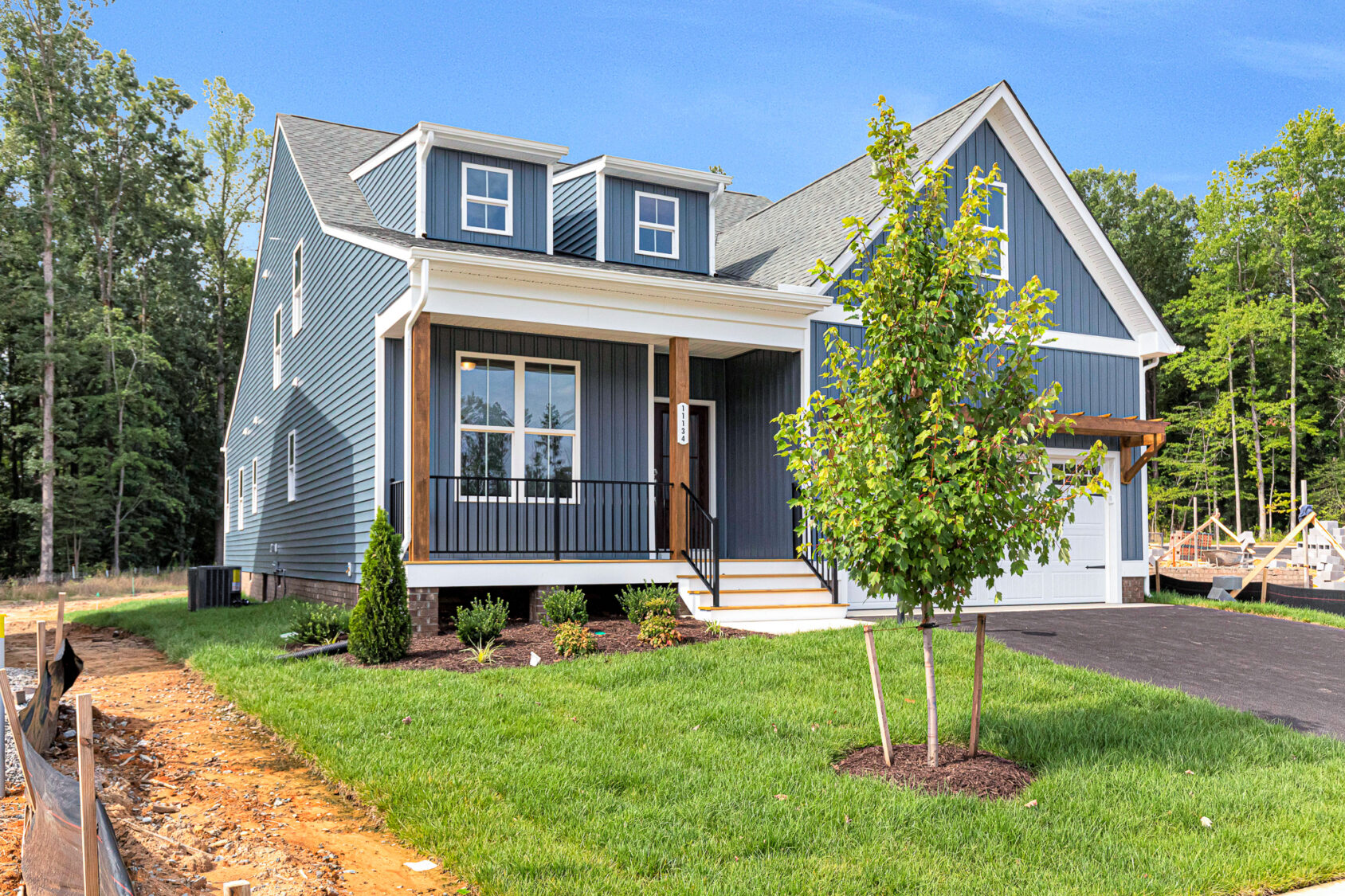 Charming blue house with white trim on Somerset Hill Lot 8, featuring a porch, lawn, young tree, and driveway.