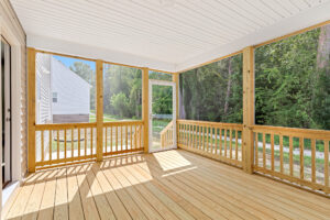 Screened-in porch with wooden floor, nestled among trees on Lot 7 in Poplar Village, near a charming white house.