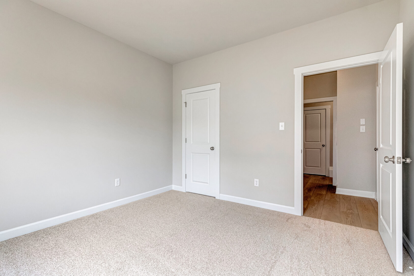 Empty beige carpeted room, two white doors, light gray walls; hallway visible—located in Poplar Village Lot 7.