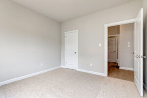 Empty beige carpeted room, two white doors, light gray walls; hallway visible—located in Poplar Village Lot 7.