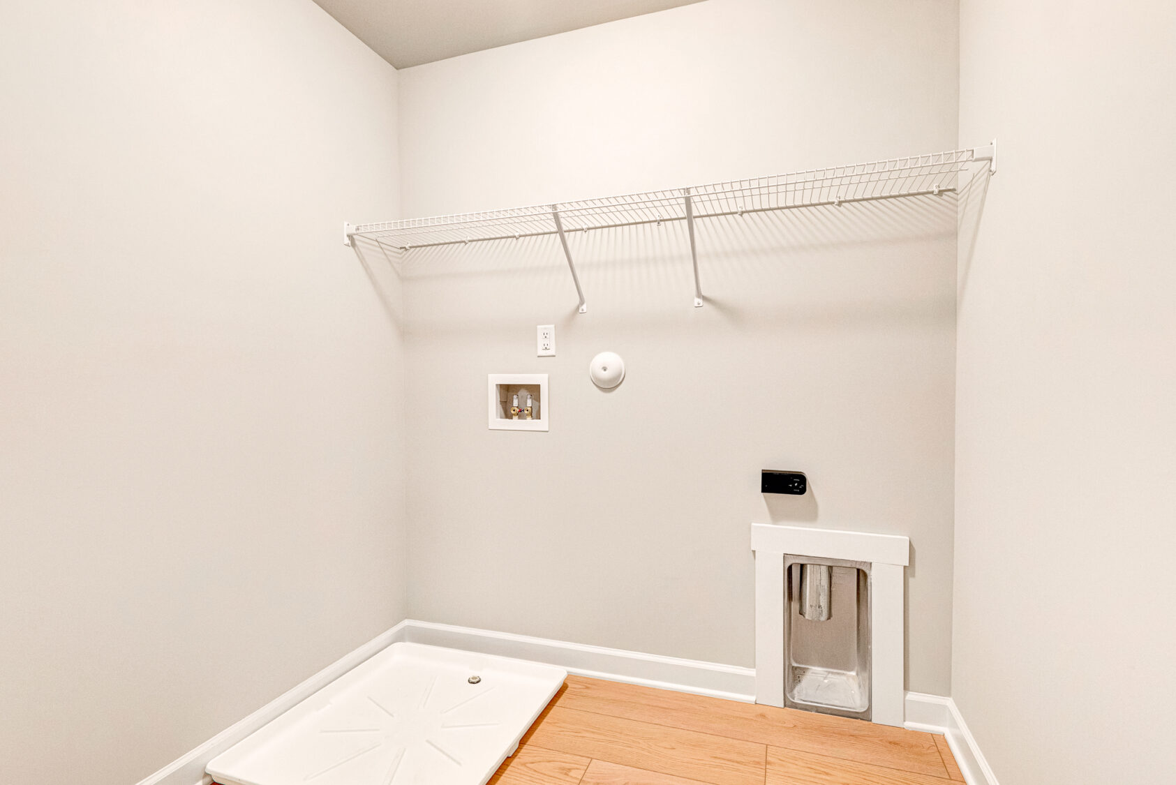 Empty laundry room in Poplar Village’s Lot 7 with a wire shelf, washer tray, outlets, and wooden flooring.