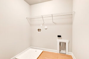 Empty laundry room in Poplar Village’s Lot 7 with a wire shelf, washer tray, outlets, and wooden flooring.