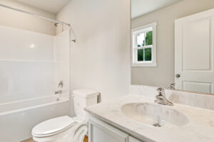 White bathroom in Poplar Village with bathtub, marble sink, and window. Experience Lot 7’s natural light charm.