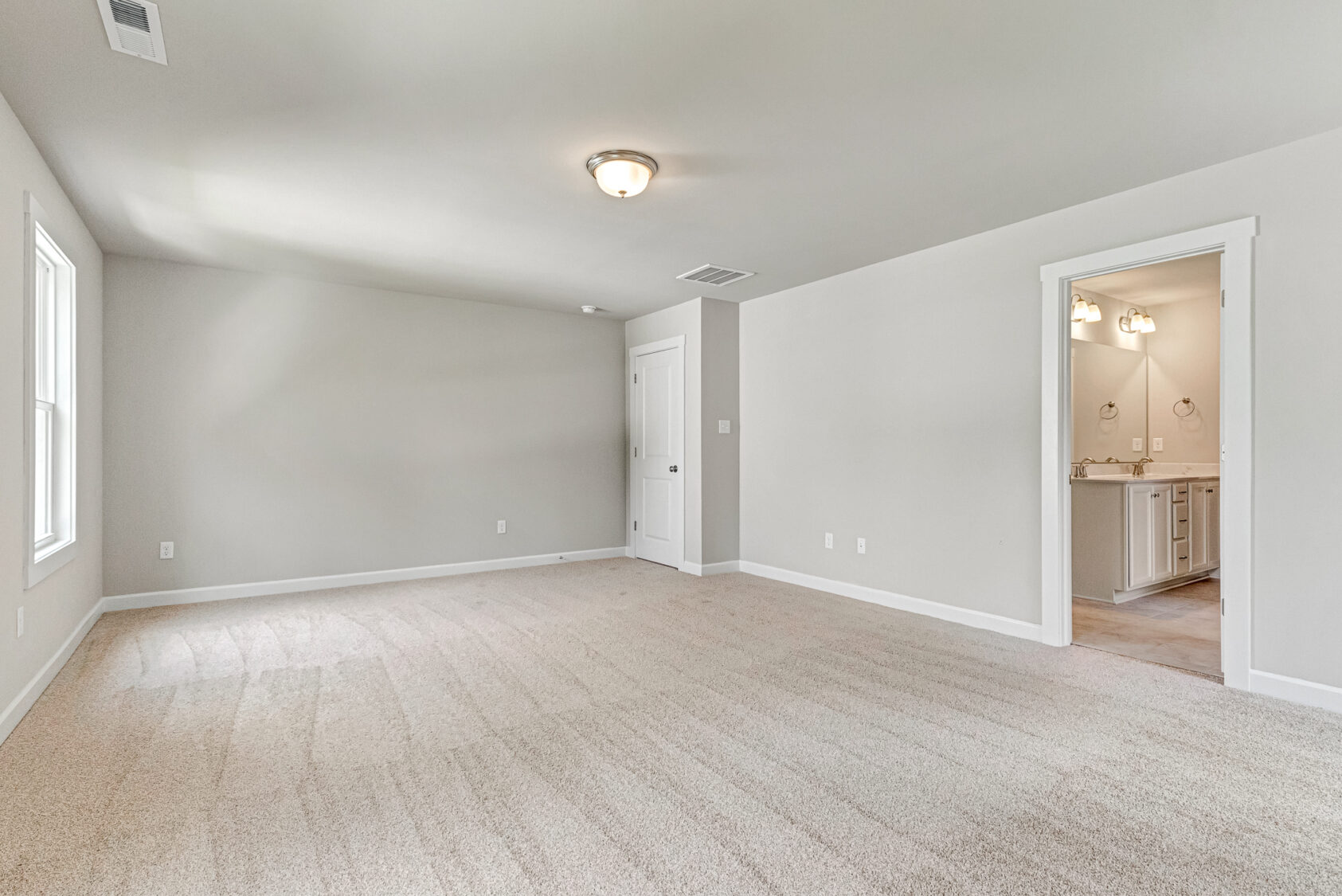 Spacious, empty room with beige carpet at Poplar Village Lot 7; window offers a view into an adjoining bathroom.