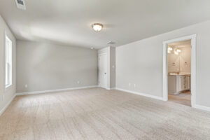 Spacious, empty room with beige carpet at Poplar Village Lot 7; window offers a view into an adjoining bathroom.