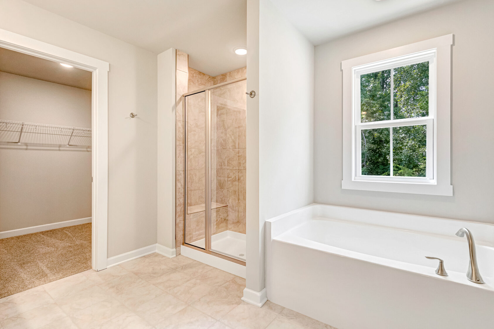 Bathroom in Lot 7, Poplar Village, features a white tub, glass shower, window, and carpeted open closet with wire shelves.