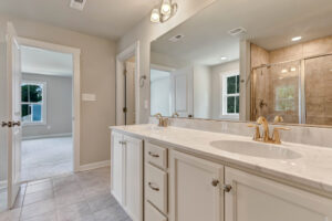 Modern bathroom in Poplar Village Lot 7 with marble double sink, gold faucets, large mirror, and glass shower enclosure.