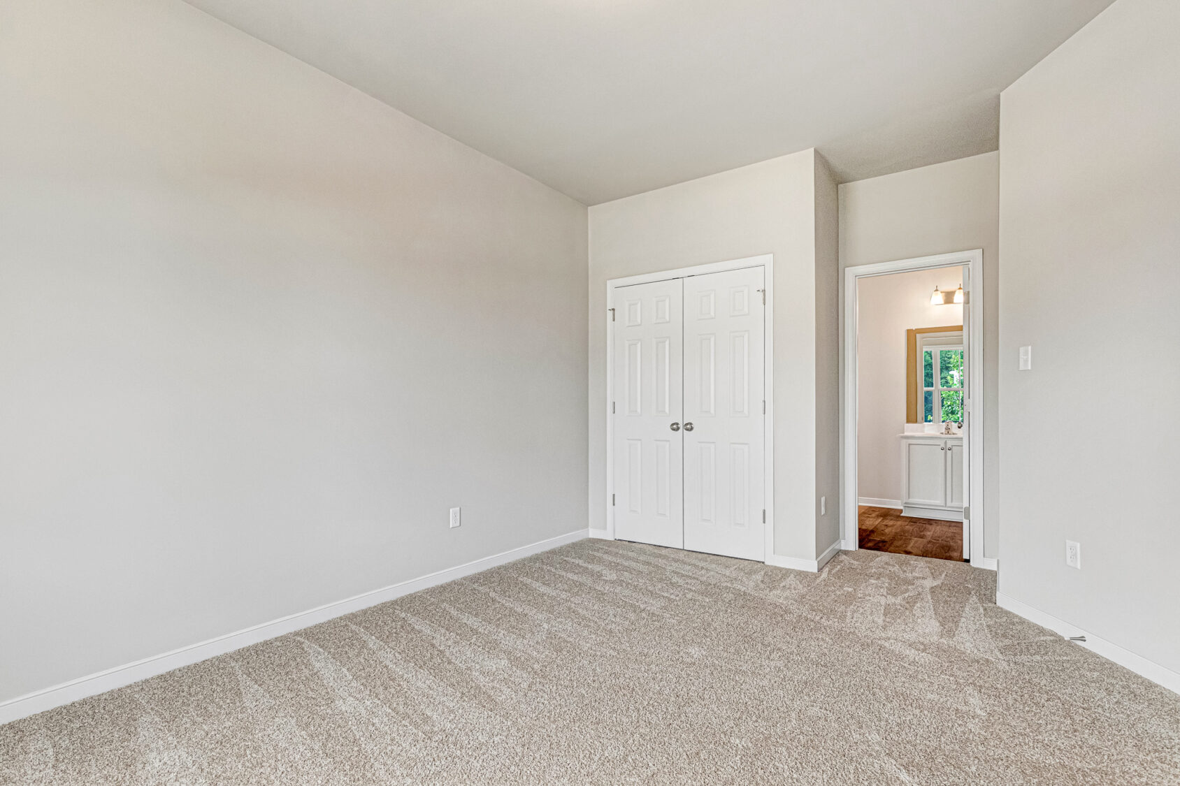Empty Somerset Hill room with beige carpet, white walls, double closet doors, and view into hallway with light fixture.