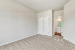 Empty Somerset Hill room with beige carpet, white walls, double closet doors, and view into hallway with light fixture.