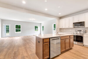 Modern kitchen in Lot 8, Somerset Hill features white cabinets, island, stainless appliances, and open wood-floored living.