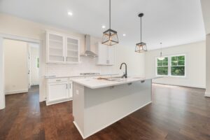 Modern kitchen with white cabinets, island, and hardwood floors in bright Lot 7 at Shirley Commons.