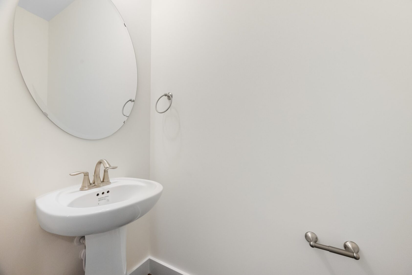 Small bathroom at Shirley Commons, Lot 7, with a white pedestal sink, oval mirror, and an empty towel ring.