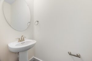 Small bathroom at Shirley Commons, Lot 7, with a white pedestal sink, oval mirror, and an empty towel ring.