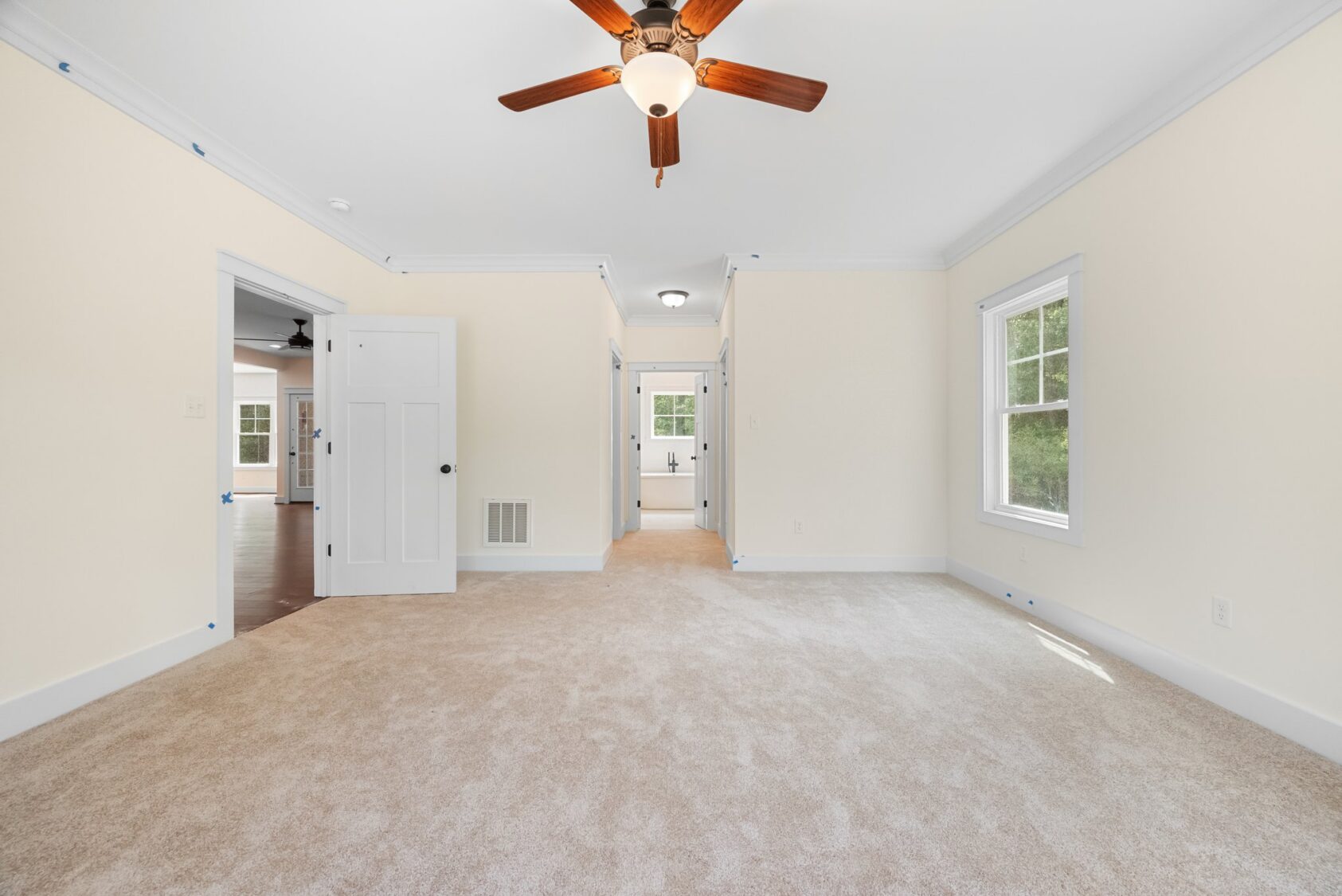Bright, carpeted room at Shirley Commons with beige walls, ceiling fan, two windows, and doors to Lot 7.