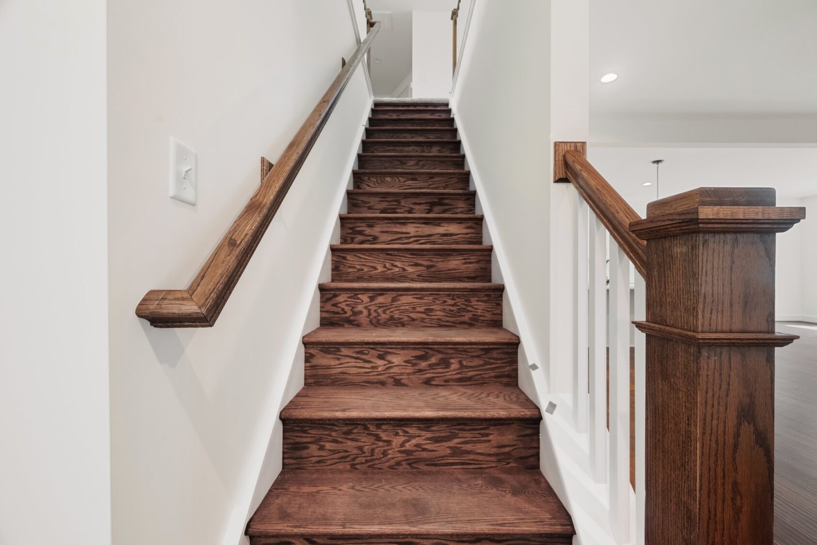 A staircase with dark wooden steps and a wooden handrail leads upward in Lot 7 at Shirley Commons.