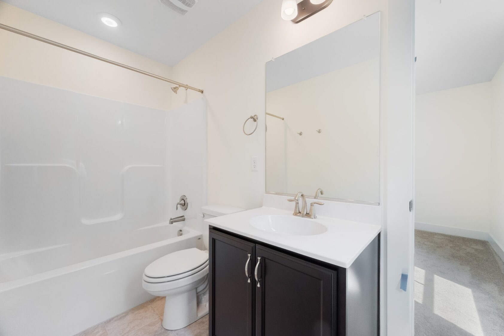 Modern bathroom in Shirley Commons Lot 7 with white tub-shower, dark vanity, large mirror, and light-colored walls.