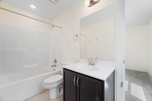 Modern bathroom in Shirley Commons Lot 7 with white tub-shower, dark vanity, large mirror, and light-colored walls.