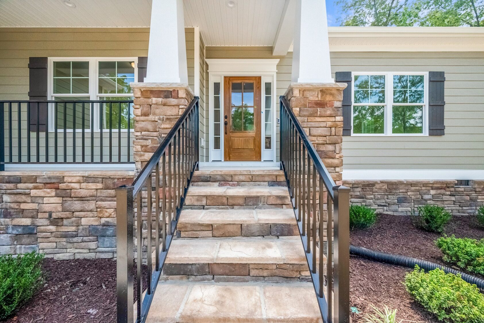 Stone steps and black railings lead to the wooden front door of Lot 7 in Shirley Commons, with white trim and columns.