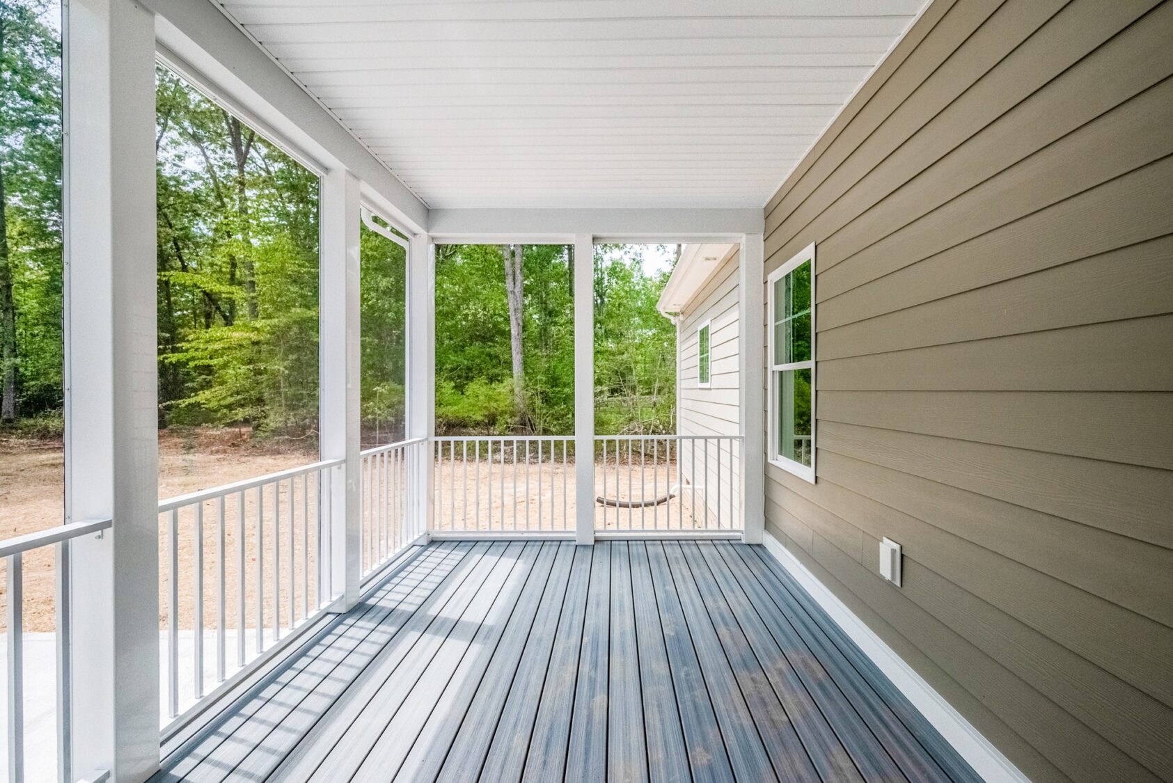 Screened-in porch at Shirley Commons Lot 7 with gray flooring, white railing, and views of trees and greenery outside.