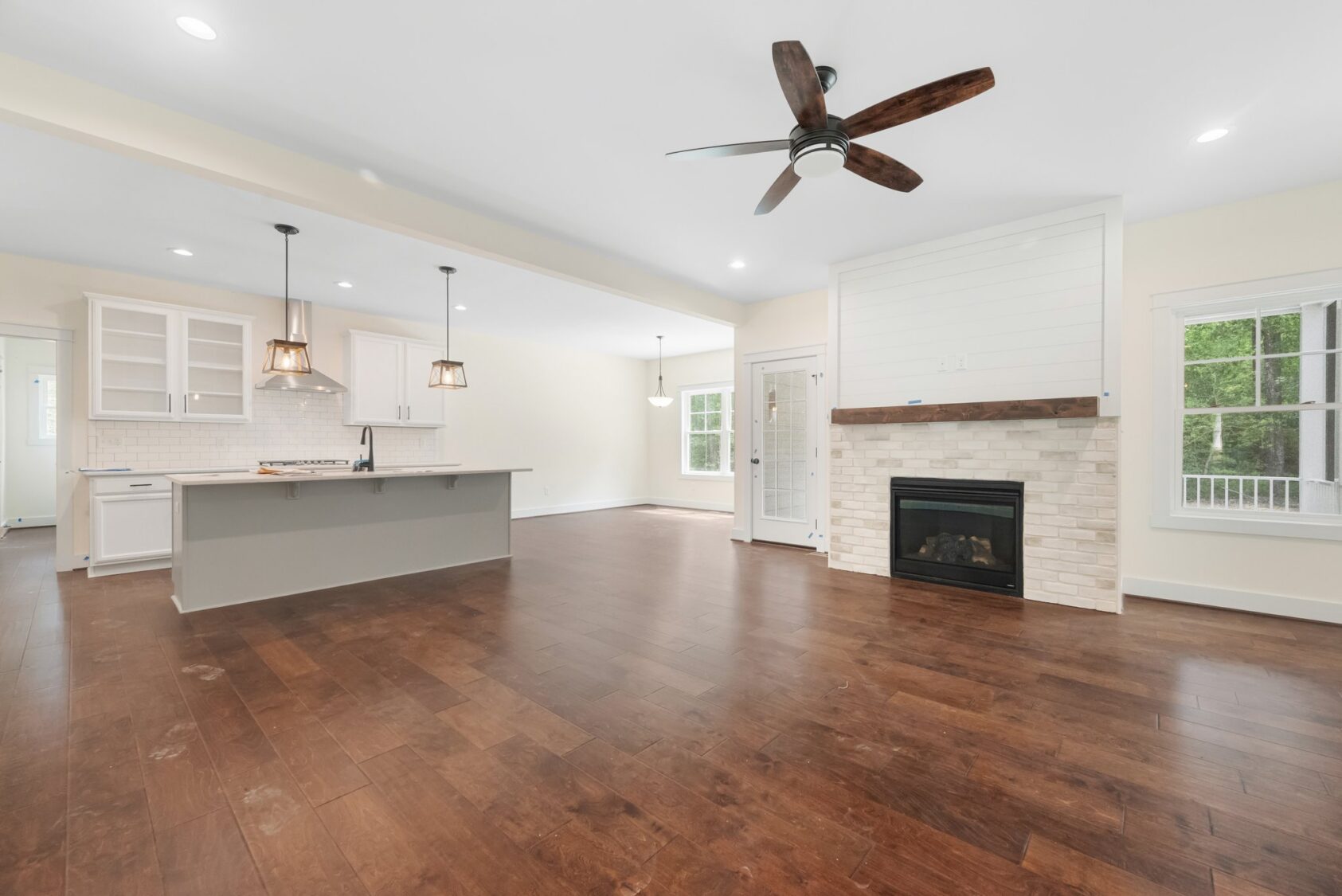 Spacious open kitchen and living area in Shirley Commons features wood floors, white cabinets, and a fireplace with mantel.