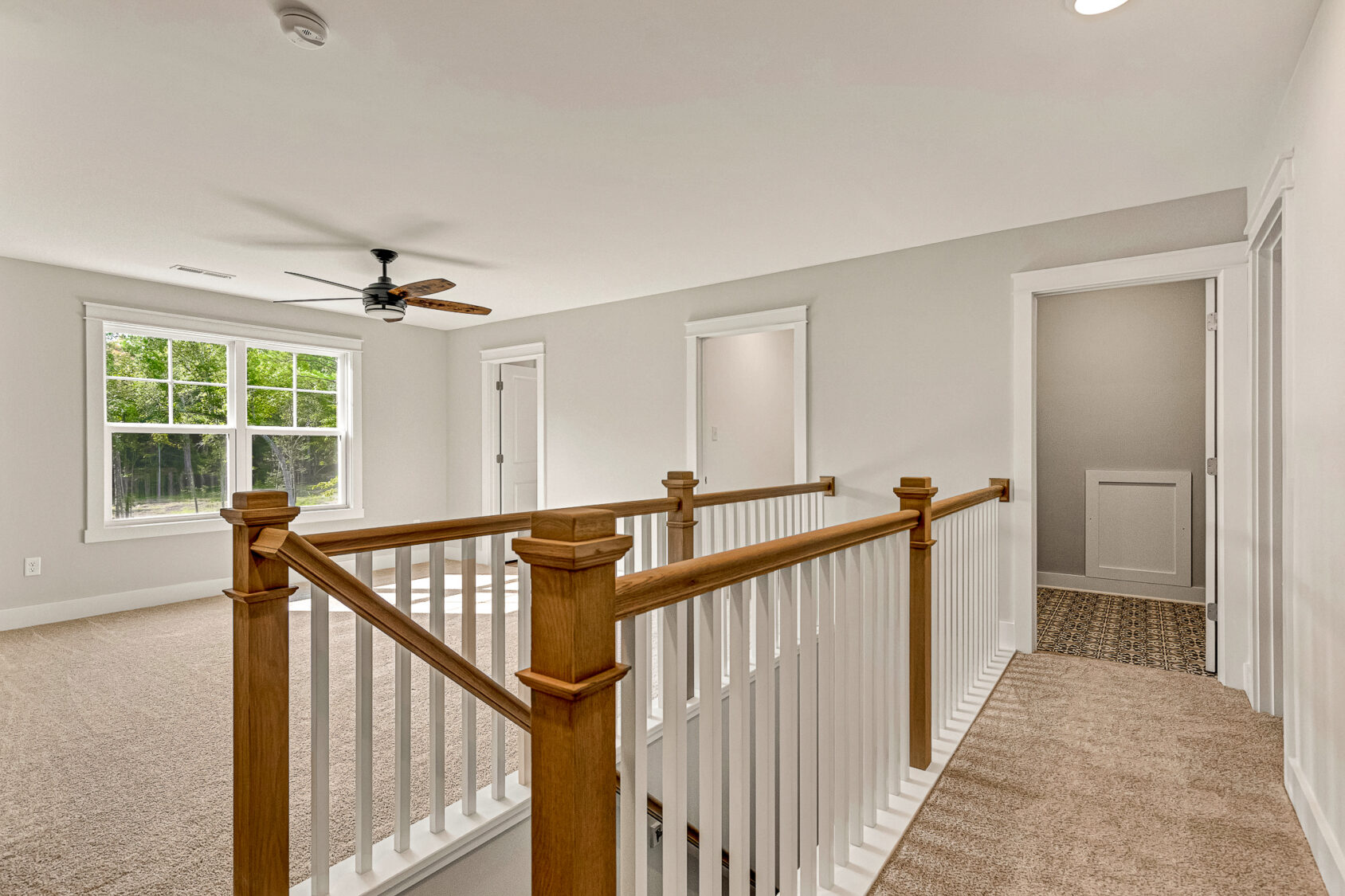 Upstairs hallway in Somerset Hill Lot 7 with beige carpet, white walls, wooden railing, and natural light from a window.