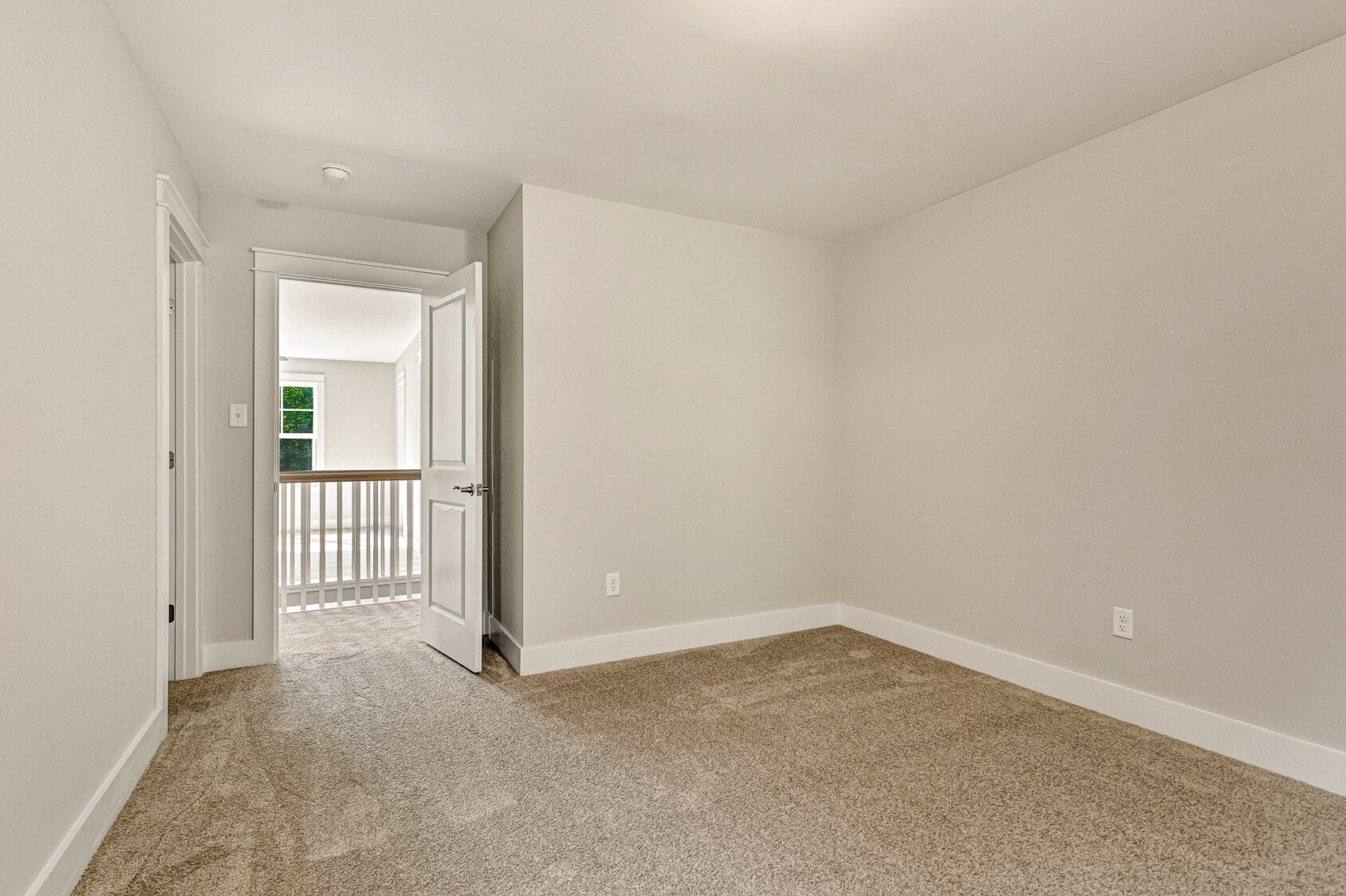 Empty beige carpeted room with white walls, open door, and natural light in Somerset Hill’s Lot 7 hallway.
