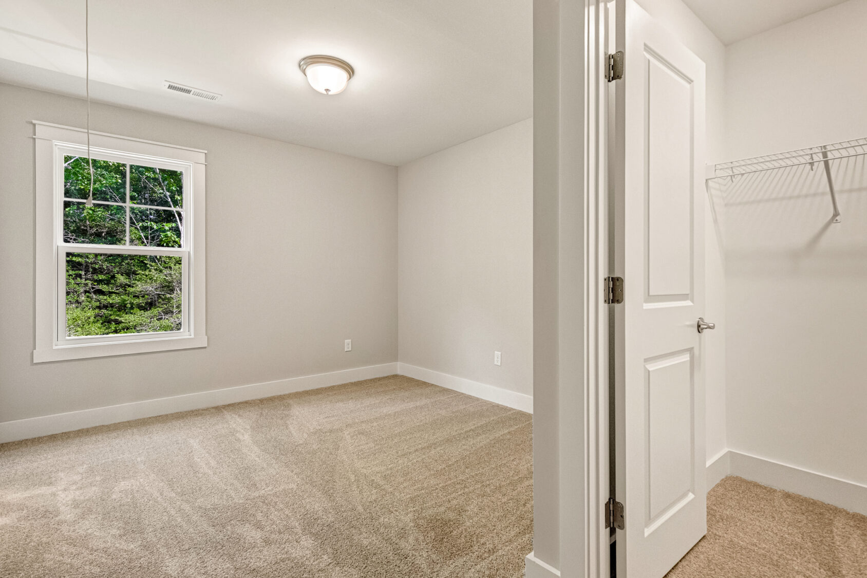 Empty carpeted bedroom in Somerset Hill, Lot 7, with window, ceiling light, and closet with a wire shelf.
