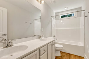 Bright Somerset Hill bathroom with double sink vanity, large mirror, tub/shower, wood floor. Lot 7.