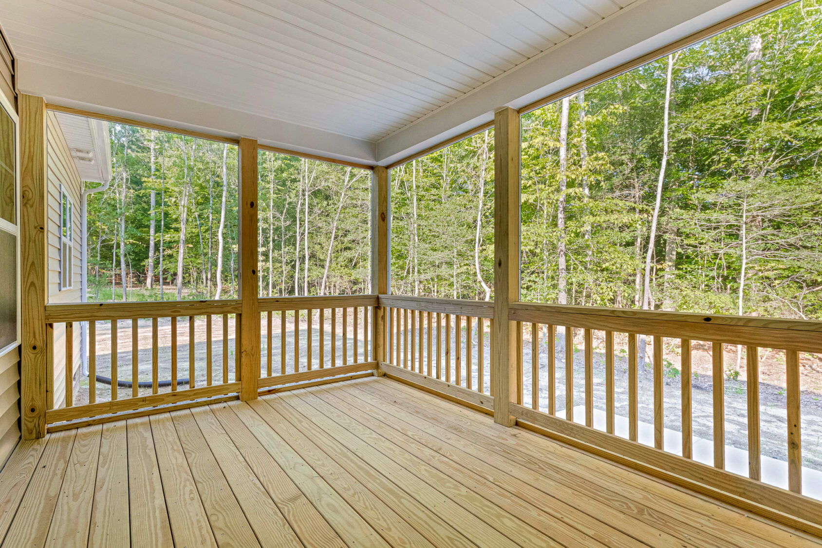 A wooden screened-in porch on Somerset Hill overlooks a forested area with trees and a gravel driveway.