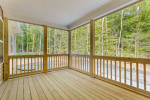 A wooden screened-in porch on Somerset Hill overlooks a forested area with trees and a gravel driveway.