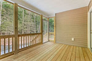 Screened-in wooden porch with railing at Somerset Hill Lot 7, overlooking woods and featuring a door to the outside.