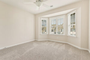 Bright empty room in Somerset Hill with beige carpet, white walls, bay windows, and a ceiling fan.