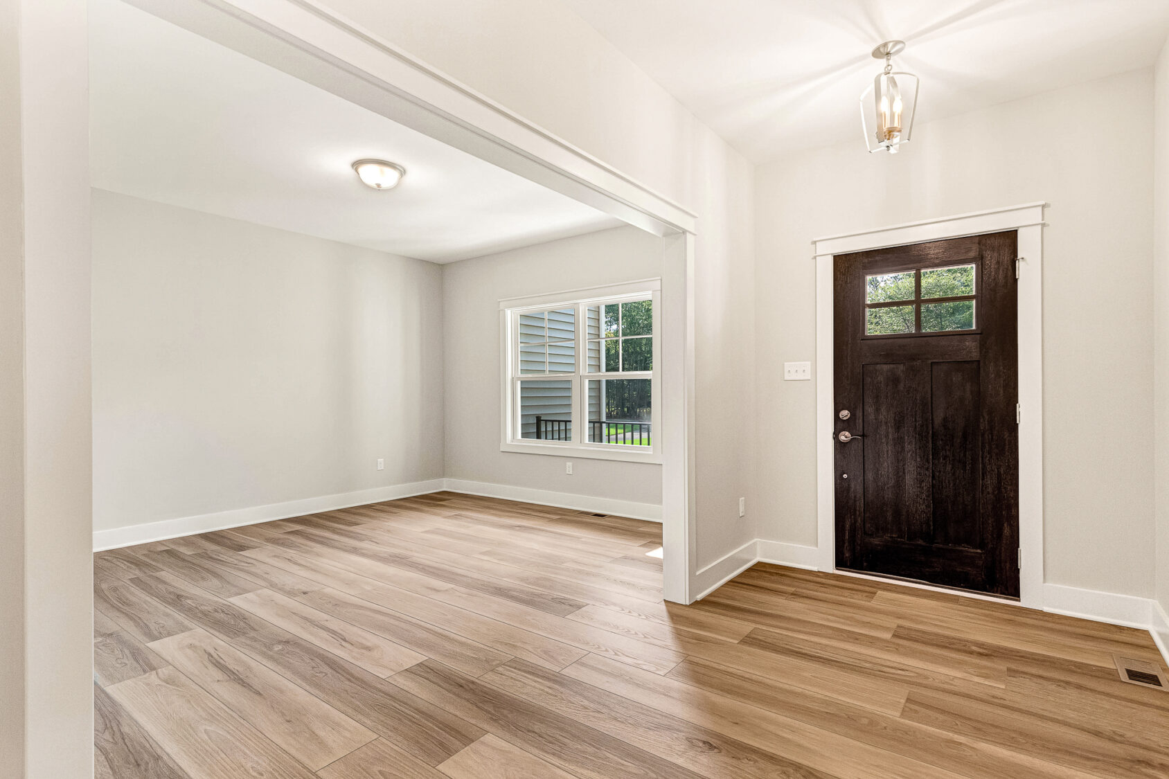 Bright Somerset Hill entryway with wood flooring, white walls, large window, and a dark wooden door with glass panels.