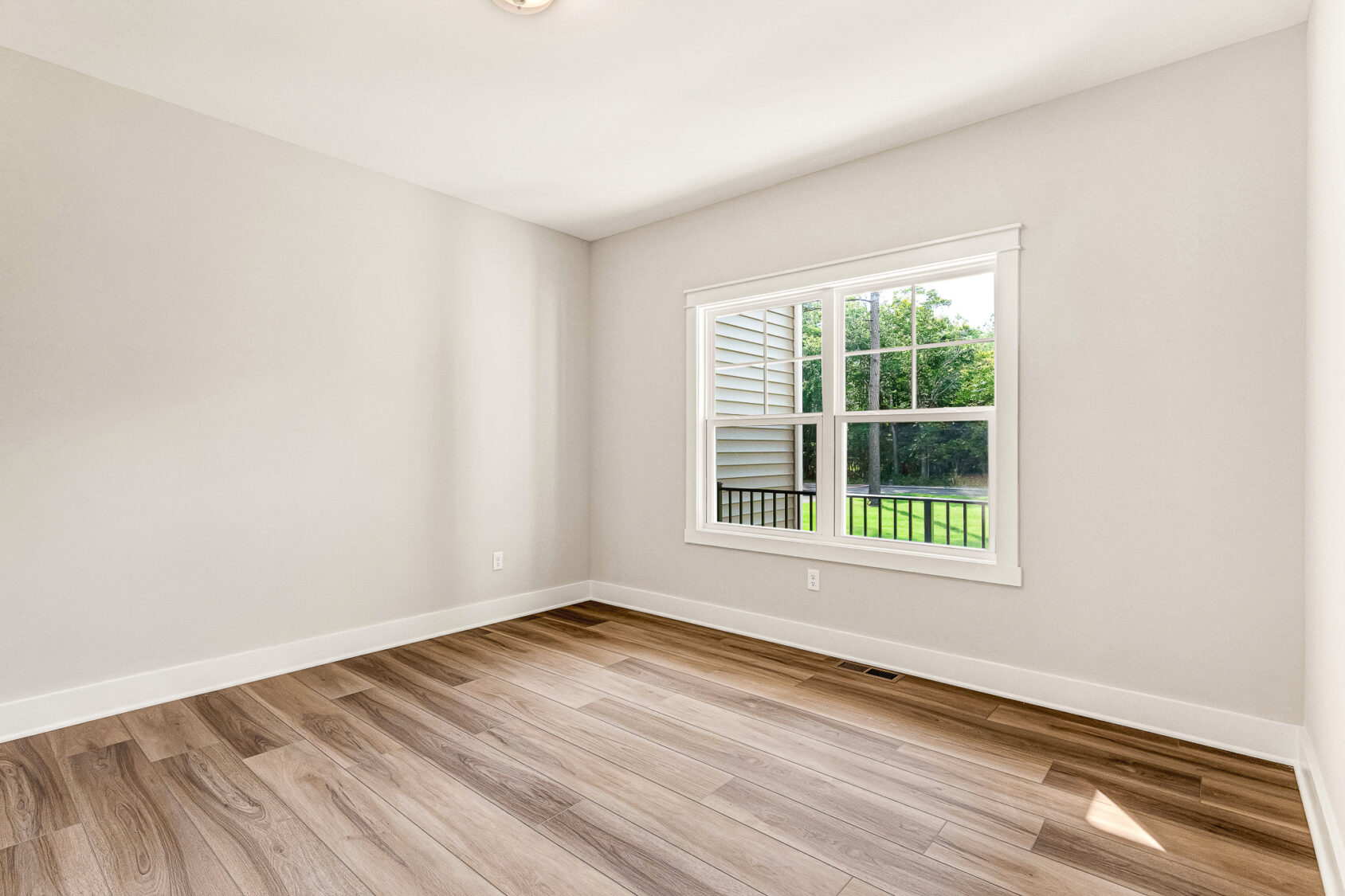 Spacious empty room in Somerset Hill, Lot 7, with light wood floors, cream walls, and a window to a green yard.