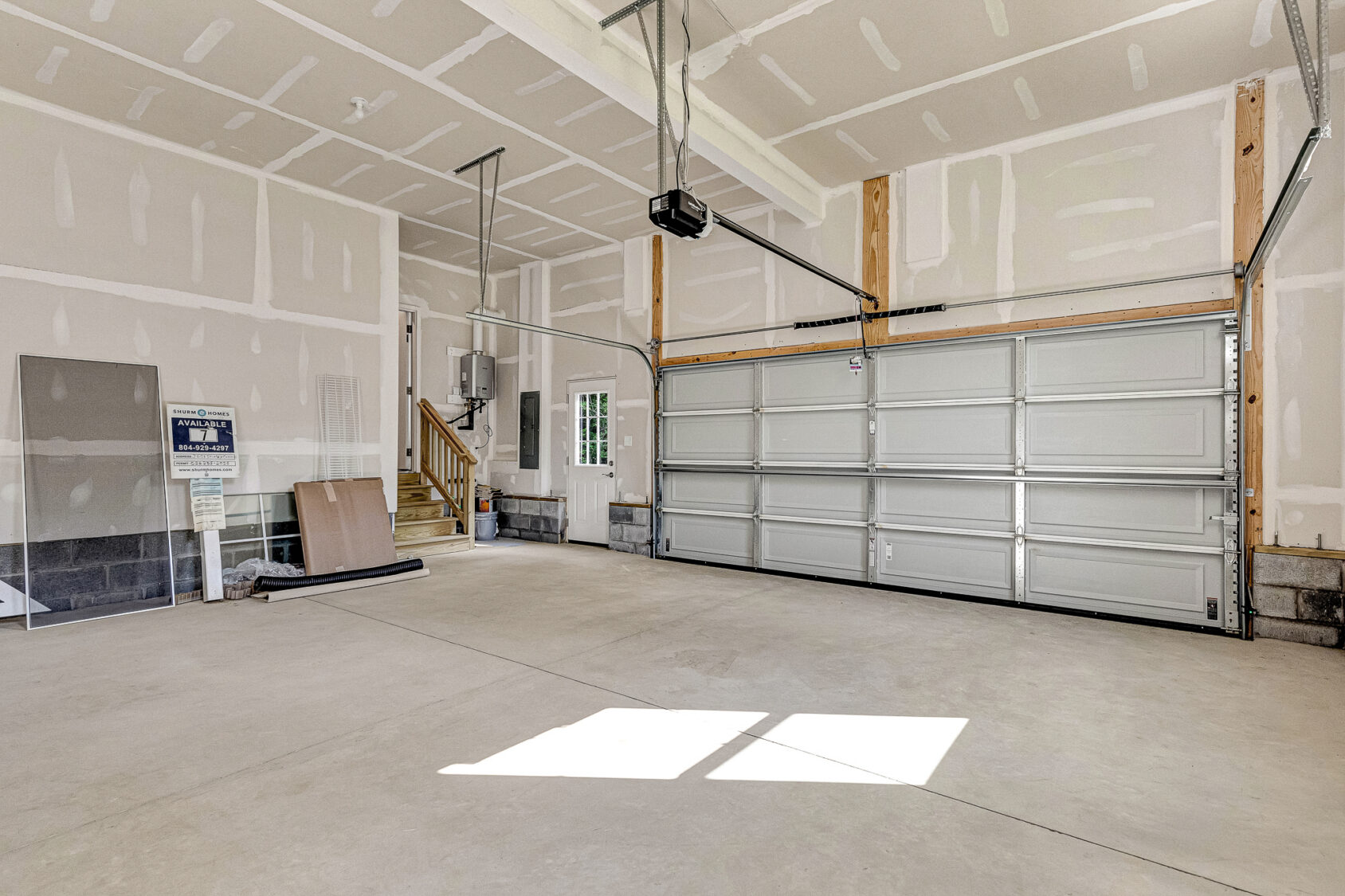 Spacious, empty two-car garage at Somerset Hill Lot 7 with unfinished walls, closed door, and items near the stairs.