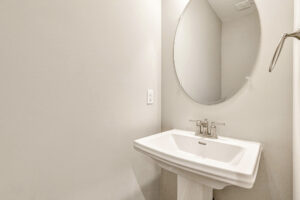A white pedestal sink with a round mirror above it adds style to the minimalist Somerset Hill Lot 7 bathroom.