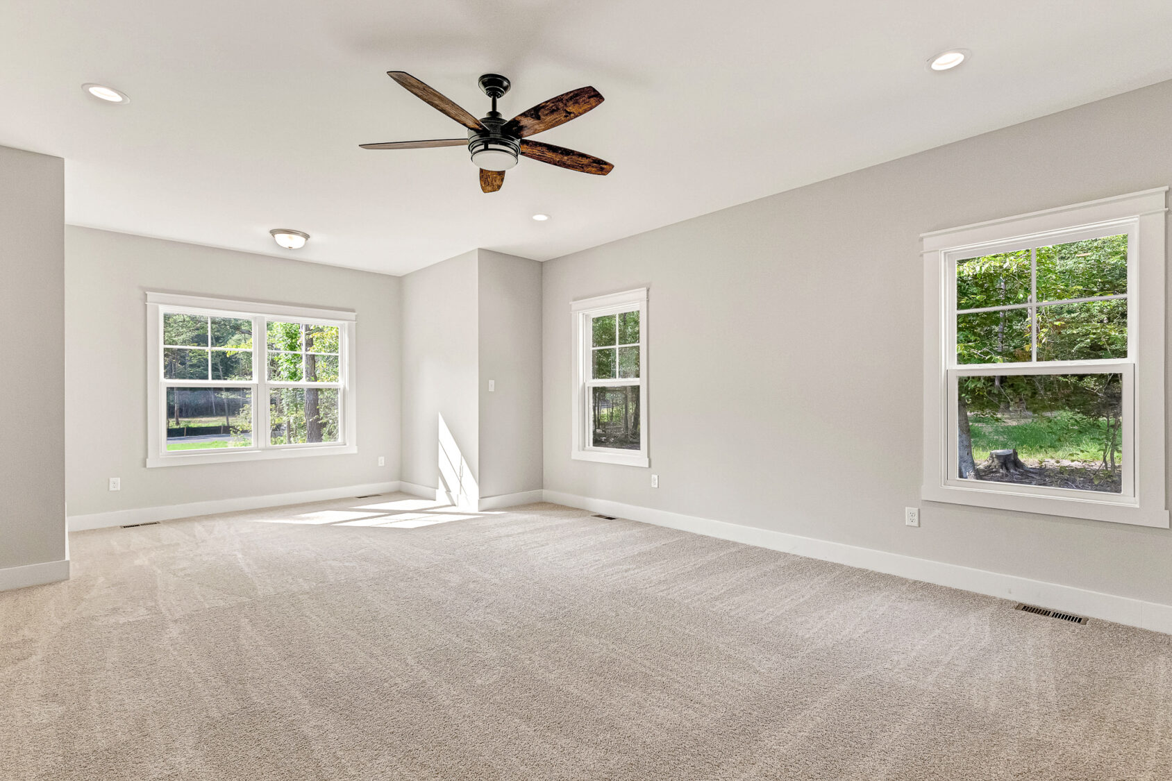 Bright empty room with beige carpet in Lot 7, Somerset Hill, large windows reveal green trees outside.
