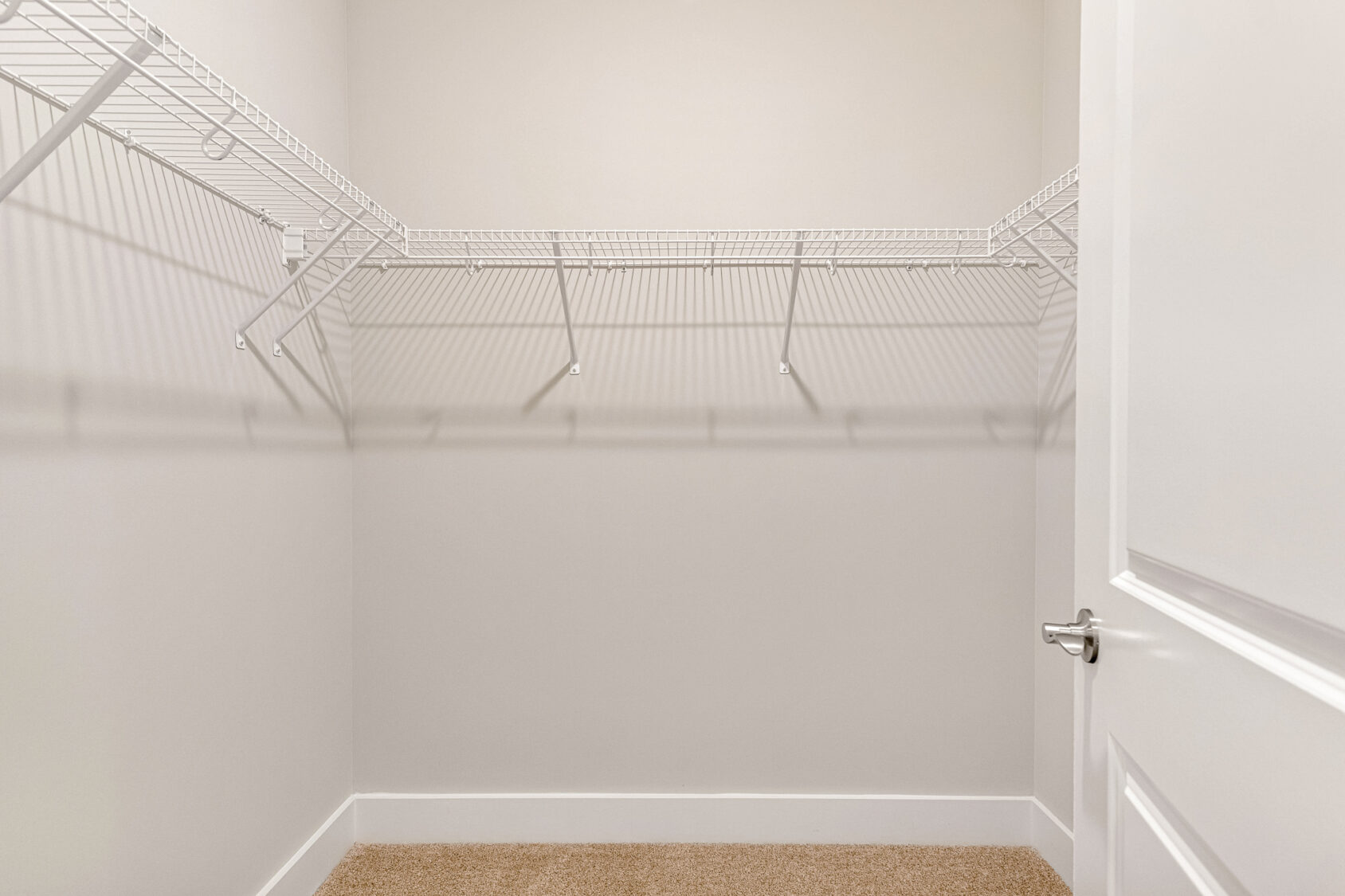 Empty walk-in closet in Lot 7, Somerset Hill; white wire shelves, beige carpet, plain walls, door slightly open right.