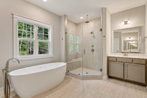 Modern bathroom at Somerset Hill Lot 7 with a freestanding tub, glass shower, double sink vanity, and scenic window views.