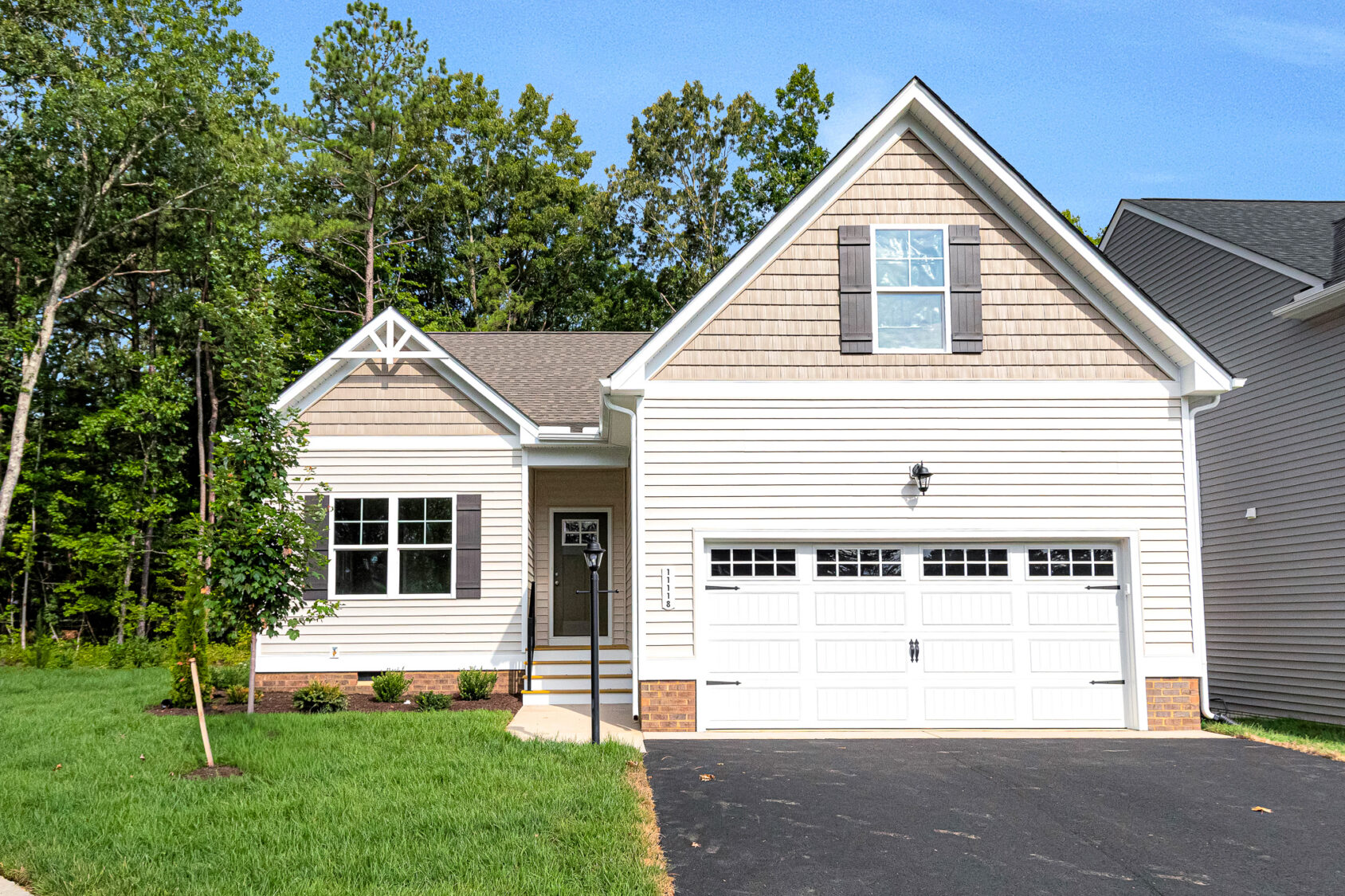 Charming single-story beige home on Somerset Hill Lot 4, with a two-car garage, green lawn, and trees behind.