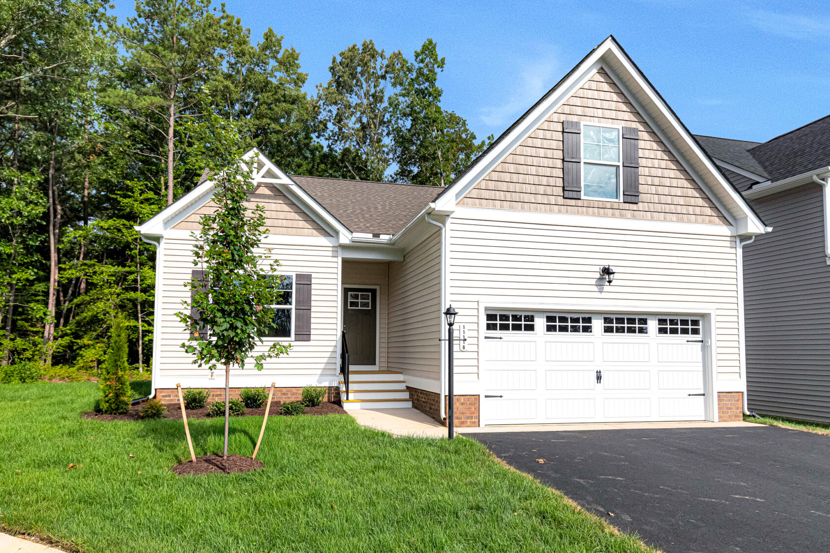 Lot 4, Somerset Hill: Light-colored suburban house with two-car garage, green lawn, and young trees on a sunny day.