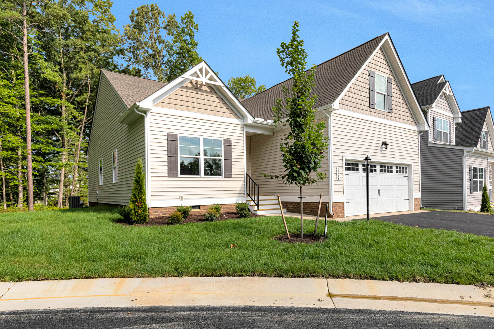 Charming single-story beige home on Somerset Hill, Lot 4, featuring black shutters and a lush yard with young trees.