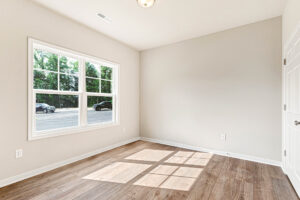 Empty room with wood floor, large window, and sunlight at Somerset Hill's Lot 4; white walls and closed door.