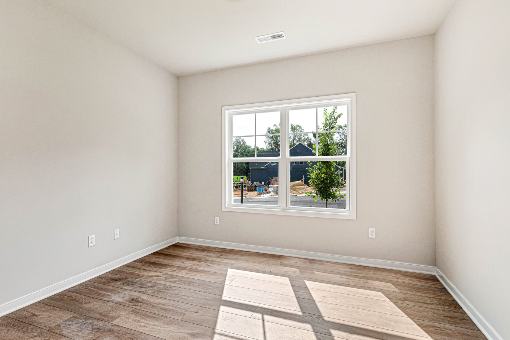 Empty room with light-colored walls, wood floor, and a large window overlooking Somerset Hill Lot 4’s sunny neighborhood.