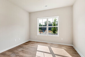 Empty room with light-colored walls, wood floor, and a large window overlooking Somerset Hill Lot 4’s sunny neighborhood.