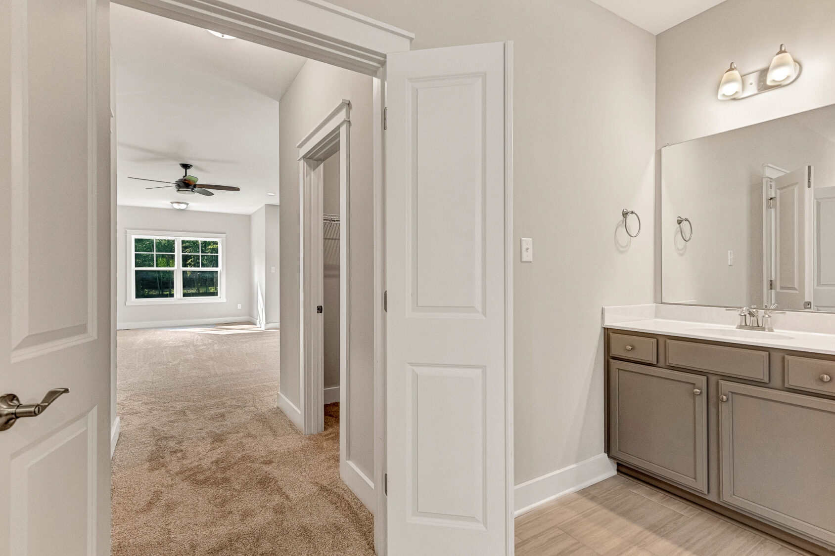 Enjoy the view from this Somerset Hill bathroom with double vanity into a carpeted bedroom with large windows and fan.