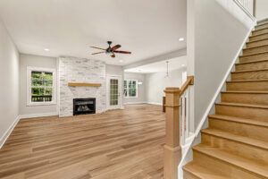 Open living room in Lot 7, Somerset Hill, with wood floors, fireplace, ceiling fan, windows, and wooden staircase.