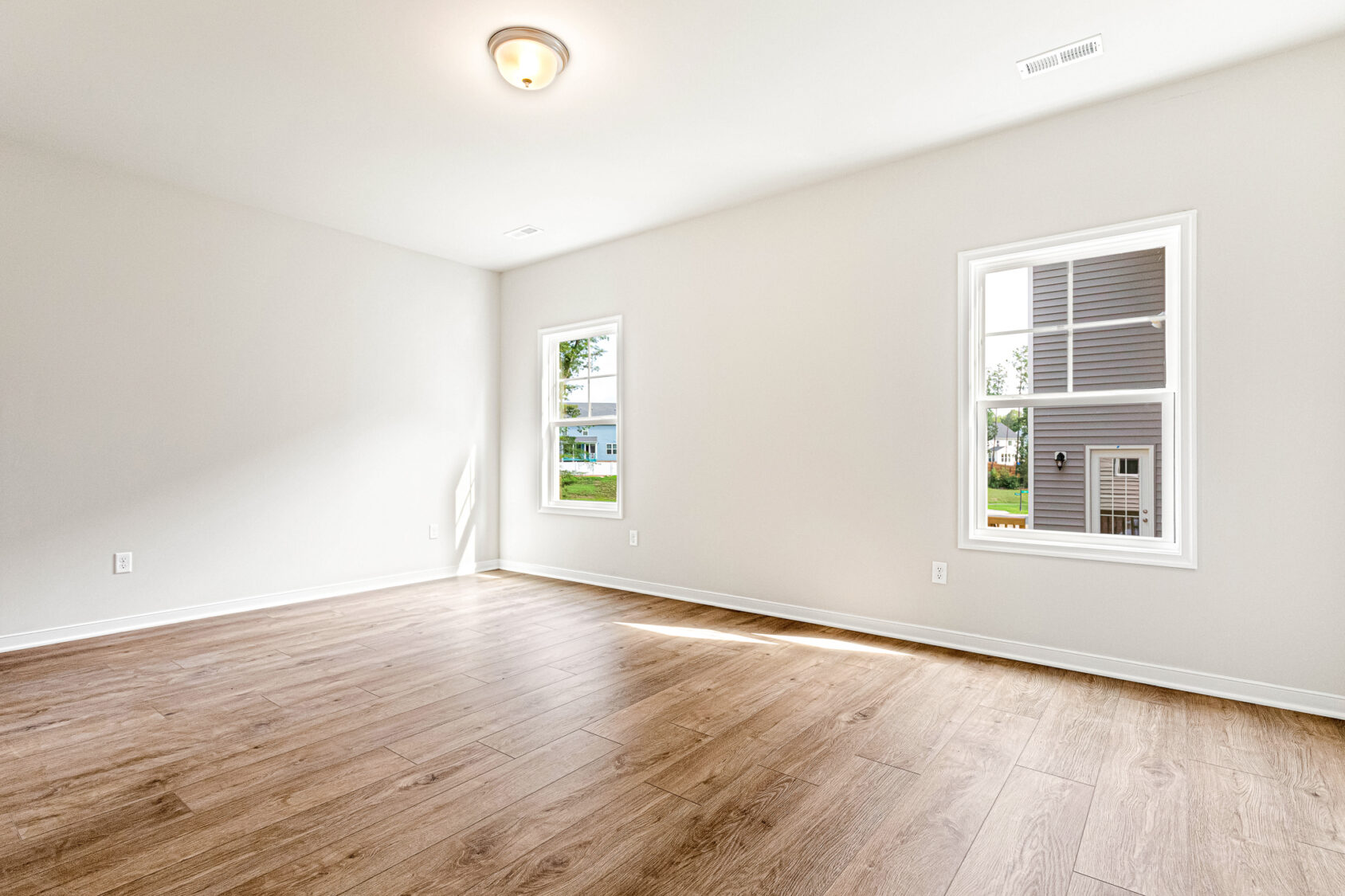 Bright empty room with wood flooring in Somerset Hill; two windows, white walls—perfect for Lot 4’s new owner.
