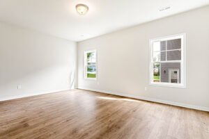 Bright empty room with wood flooring in Somerset Hill; two windows, white walls—perfect for Lot 4’s new owner.