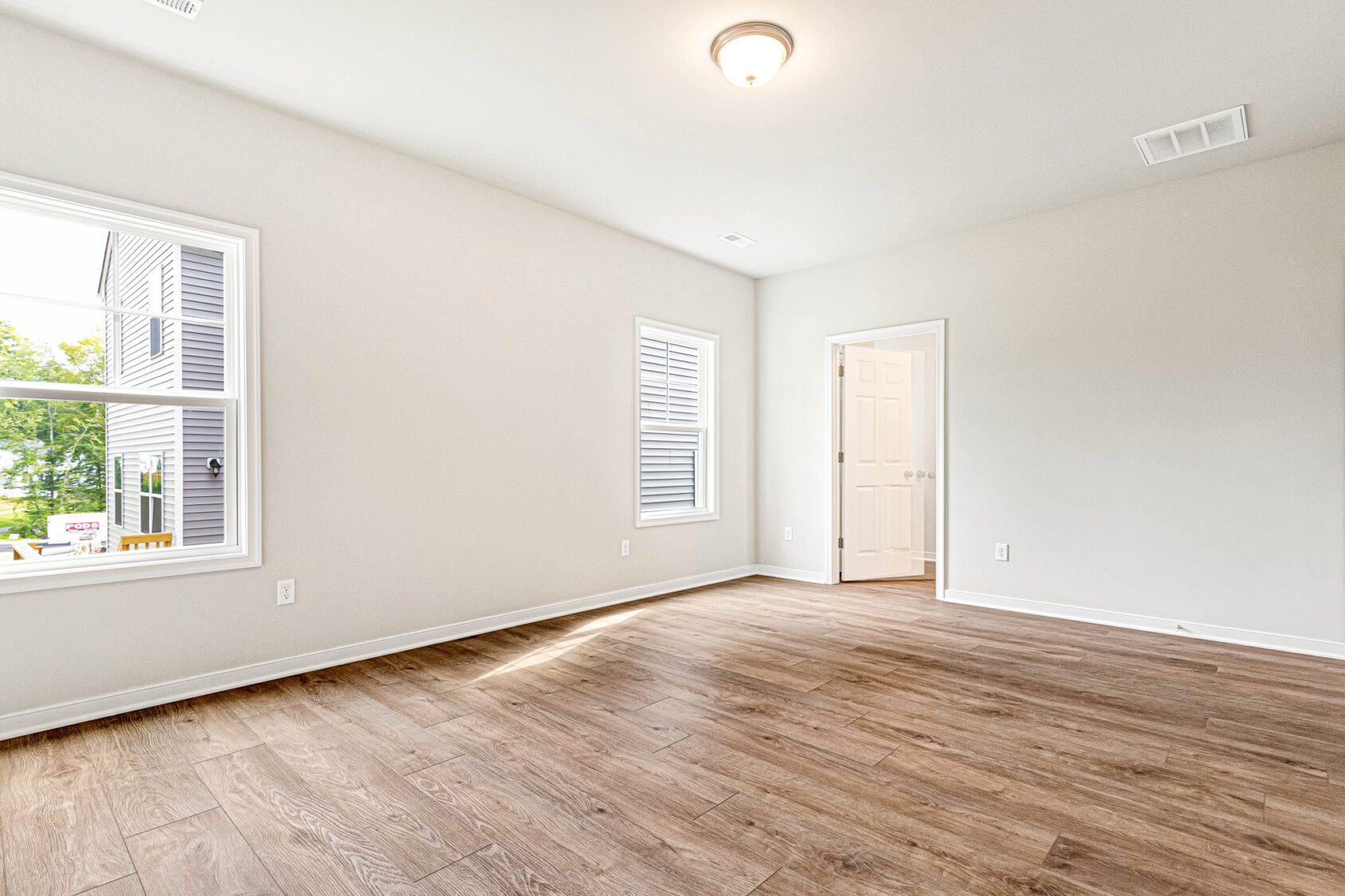 Bright, empty room at Somerset Hill Lot 4 with wood flooring, light walls, two windows, ceiling light, and open door.